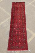 A Persian rich red ground wool runner with a floral medallion design and black borders, 33" x 116"