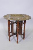 An antique Indian copper and brass tray table, on a folding turned wood base, with repousse lion and