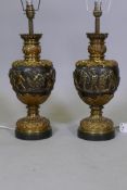 A pair of bronze table lamps with polished highlights and raised decoration depicting a procession