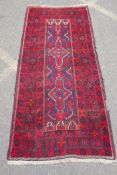 A Turkish deep red ground wool rug, with geometric designs on a central deep blue cartouche, 100 x