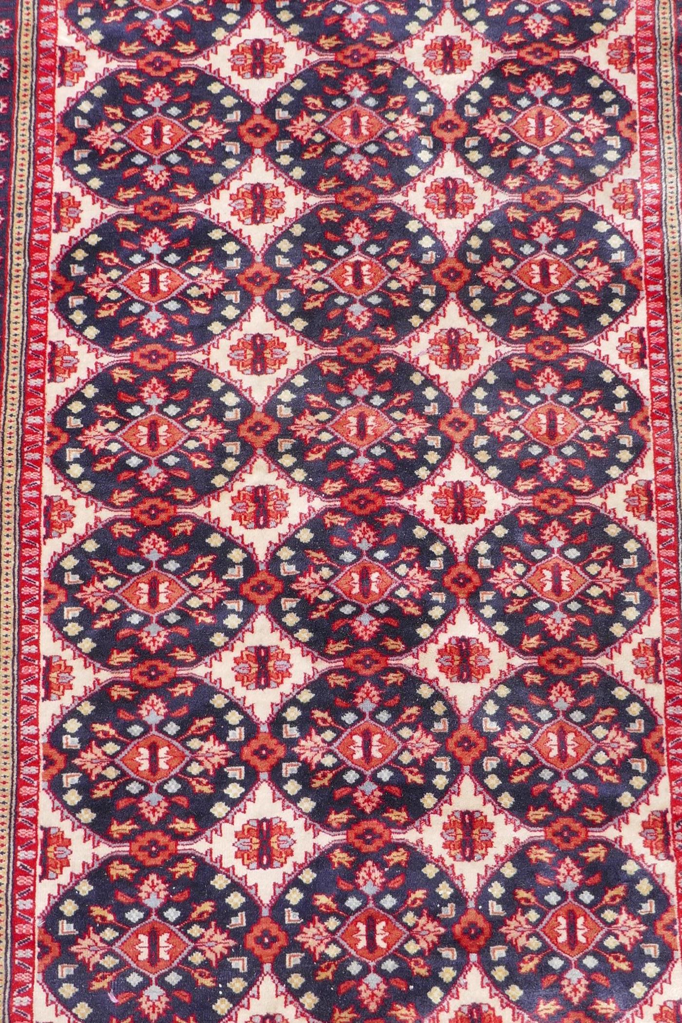 A Persian wool rug with Bokhara style medallion design and blue borders, 125cm x 180cm - Image 2 of 4
