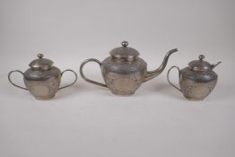 An Indian white metal three piece tea set with chased scrolling decoration, largest 29 cm long