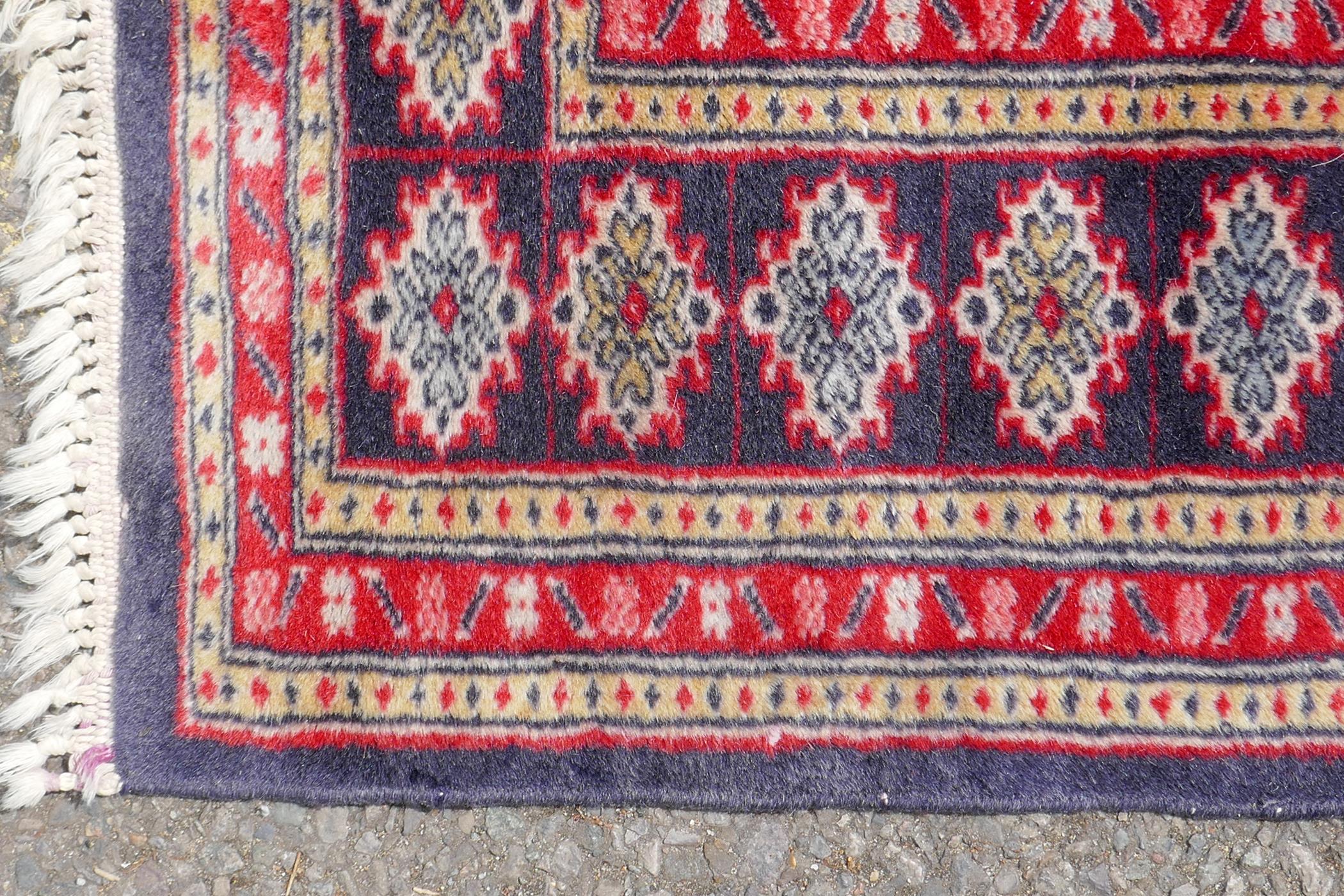 A Persian wool rug with Bokhara style medallion design and blue borders, 125cm x 180cm - Image 3 of 4