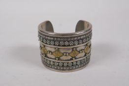 A Turkmen white metal bangle with lapiz stone ends and pressed gilt metal decoration, 7cm diameter