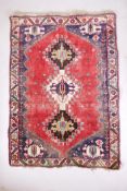 A Persian red ground hand woven wool rug with a geometric triple lozenge design, 105cm x 158cm