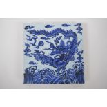 A Chinese blue and white porcelain temple tile decorated with a dragon in flight, 20cm x 20cm