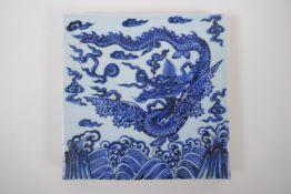 A Chinese blue and white porcelain temple tile decorated with a dragon in flight, 20cm x 20cm
