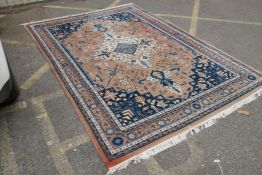 An oriental salmon pink ground wool rug with a blue geometric medallion design, 310cm x 214cm