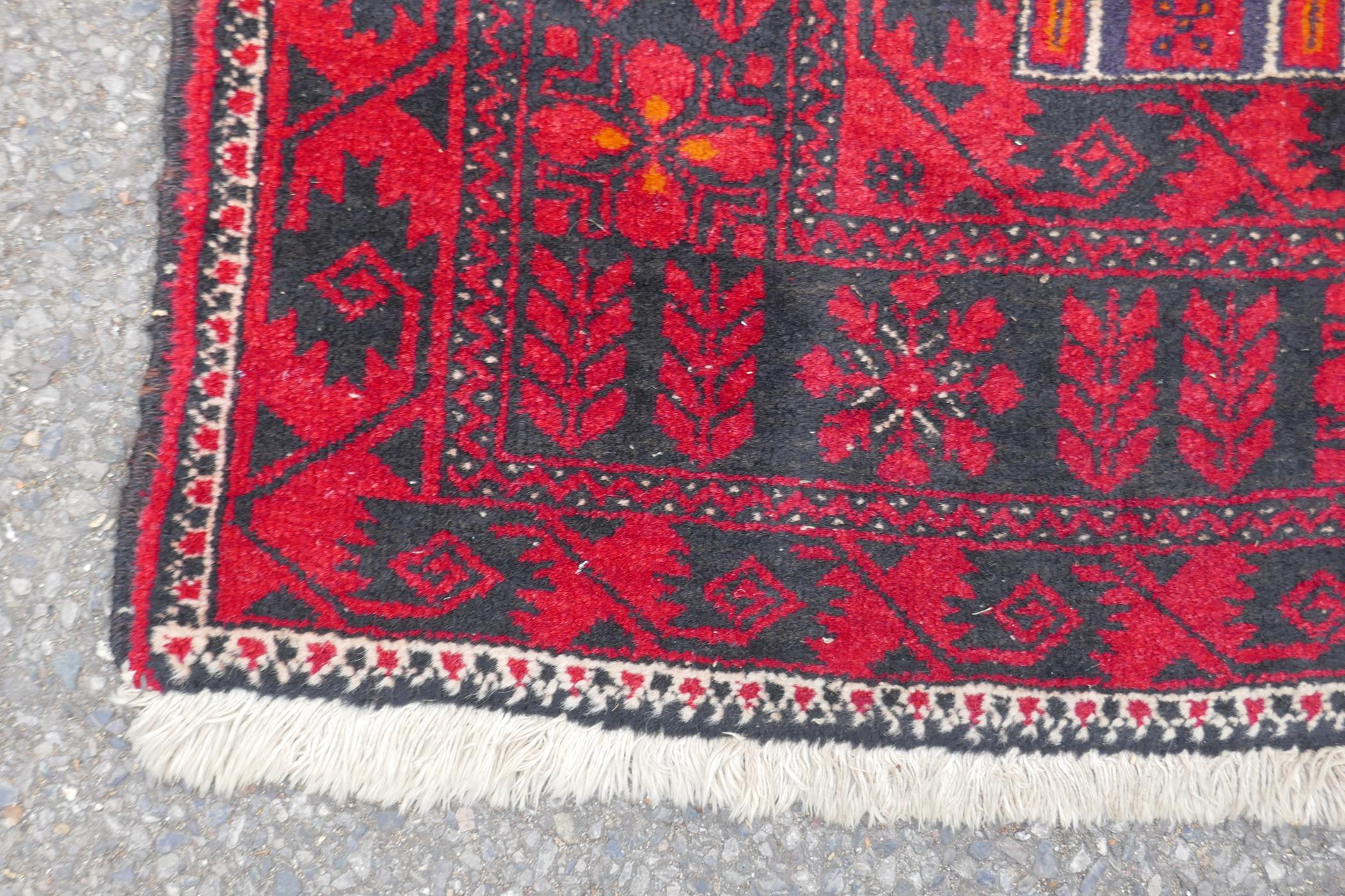 A Turkish deep red ground wool rug, with geometric designs on a central deep blue cartouche, 100 x - Image 6 of 7