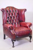 A Georgian style button back leather wing armchair, raised on cabriole supports