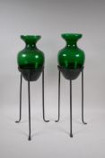 A pair of green glass vases on wrought iron stands, 56cm high