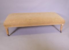 A long stool, raised on turned blond beechwood supports with brass castors, 146cm x 66cm x 47cm