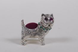 A sterling silver pin cushion in the form of a dog with an emerald set collar and ruby eyes, 3cm