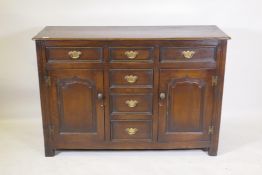 An oak dresser with three drawers and two cupboards with arched fielded panels flanking three more