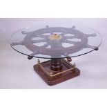 A ship's wheel glass topped coffee table on a pedestal base, with square foot and brass gallery,