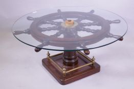 A ship's wheel glass topped coffee table on a pedestal base, with square foot and brass gallery,