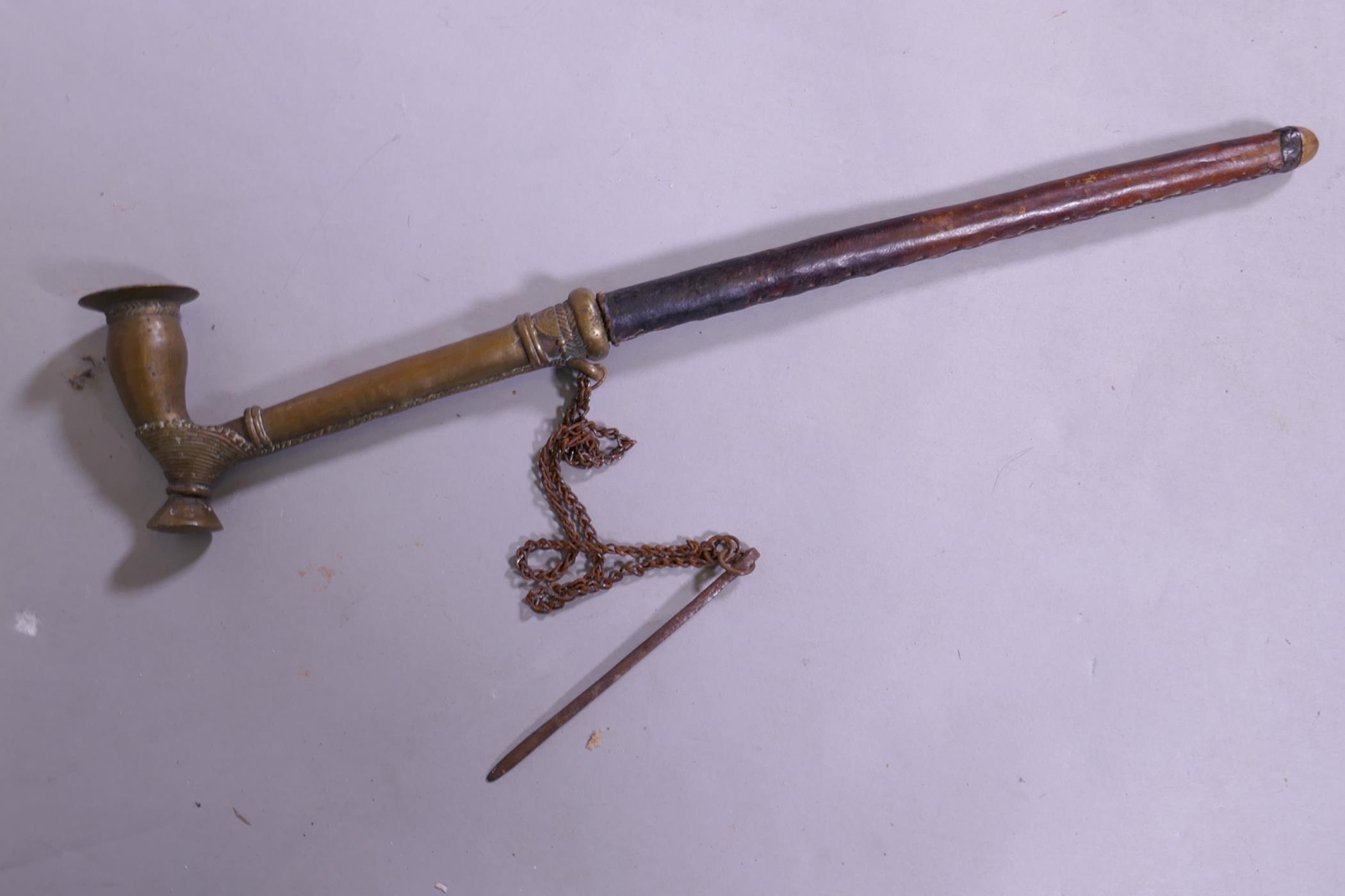 An antique Eastern bras opium pipe with stitched leather shaft, 33cm long