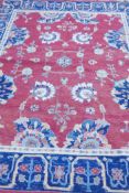 A Middle Eastern hand woven wool carpet with stylised floral designs on a faded red field, 320 x