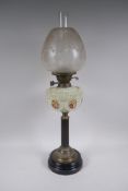 An antique brass oil lamp with a ribbed wood column, a milk glass reservoir and etched glass