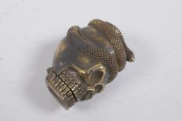 A brass vesta case in the form of skull entwined with a snake, 5cm