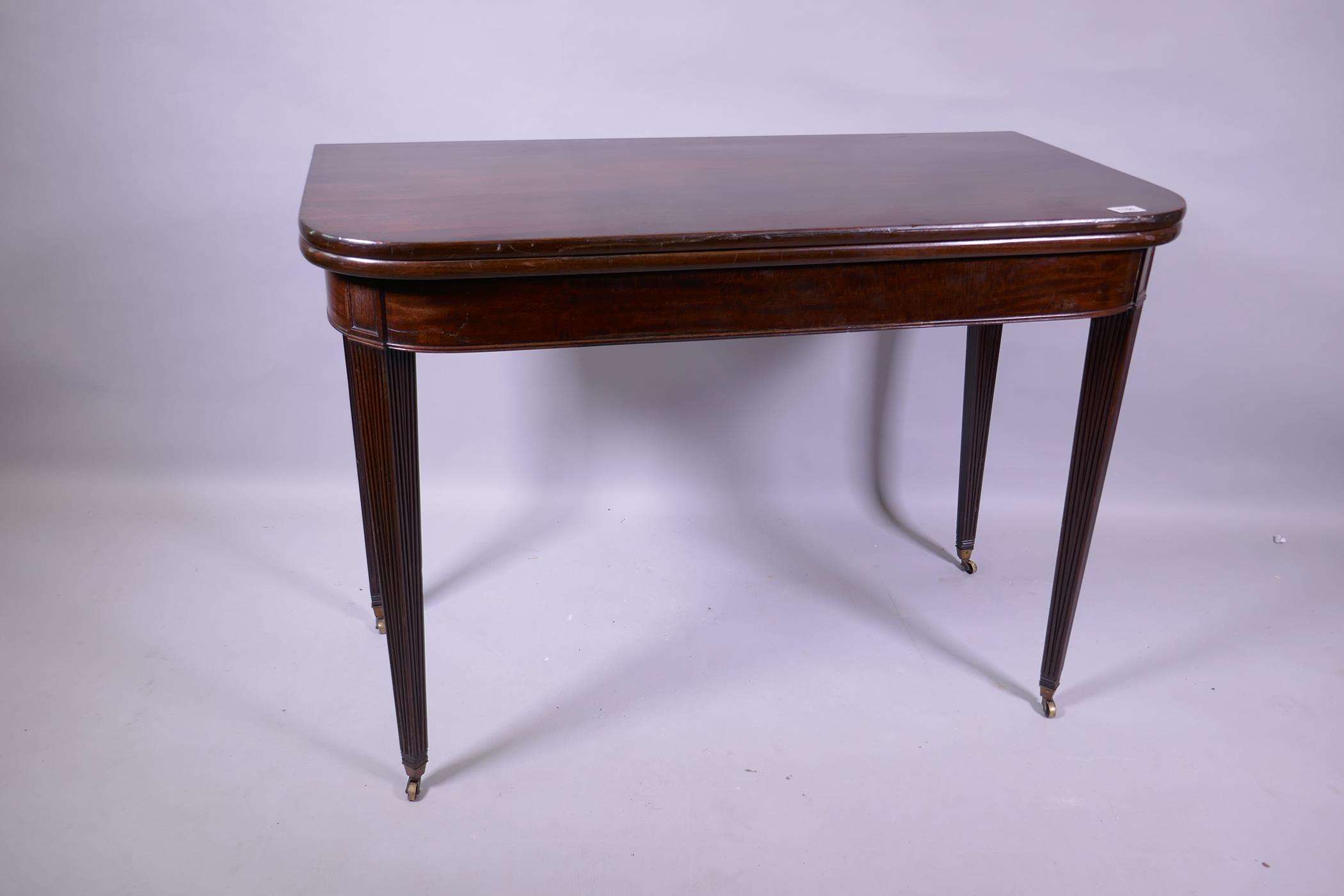 A Georgian mahogany D shaped tea table, raised on tapering reeded supports with brass castors, 102 x