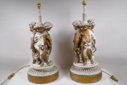 A pair of painted and parcel gilt table lamps in the form of three putti, 64cm high
