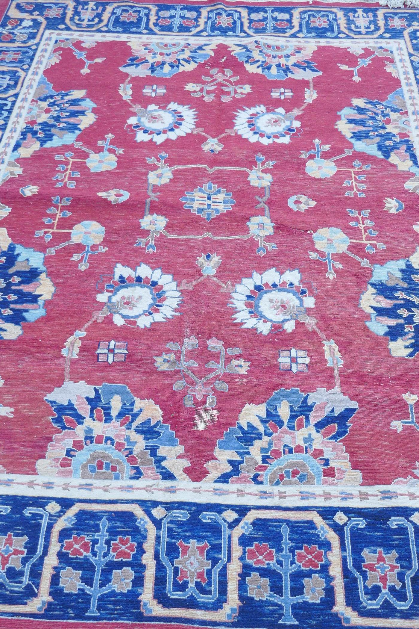 A Middle Eastern hand woven wool carpet with stylised floral designs on a faded red field, 320 x