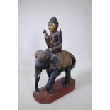 An antique south east Asian carved and lacquered wood figure of a mahout riding an elephant, with