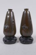 A pair of Japanese Meiji gold, silver and mixed alloy on bronze spill vases, on carved wood