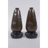 A pair of Japanese Meiji gold, silver and mixed alloy on bronze spill vases, on carved wood