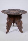 An eastern carved wood occasional table with shaped and pierced top and fold out base, AF, loss to