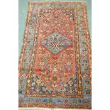 An antique Middle Eastern hand woven wool carpet with blue borders and geometric designs on a red