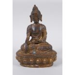 A Tibetan bronze of Buddha seated on a lotus throne, with the remnants of gilt patina