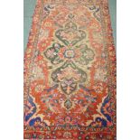 A Middle Eastern hand woven wool carpet with central floral design on a red field, 240 x 140cm