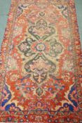 A Middle Eastern hand woven wool carpet with central floral design on a red field, 240 x 140cm