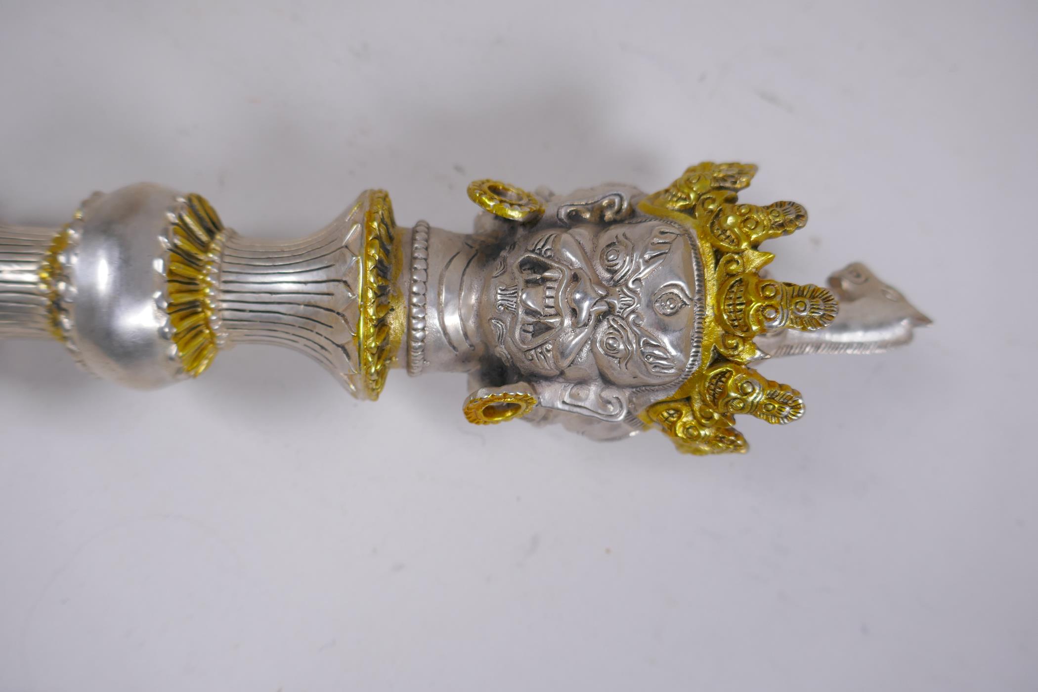 A Tibetan white metal phurba with wrathful deity mask decoration to handle and gilt highlights, 37cm - Image 2 of 2