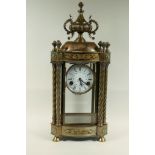 A brass mantel clock with urn finial and twisted columns, painted enamel dial and spring driven