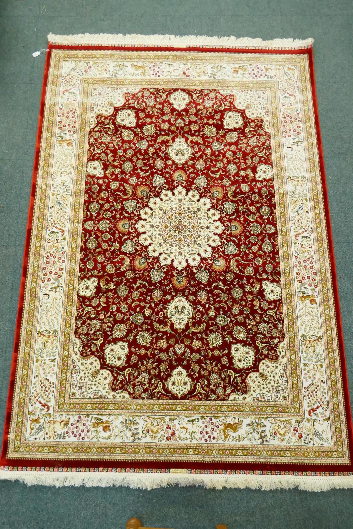 A Persian red ground full pile bamboo silk carpet with central floral medallion design and cream