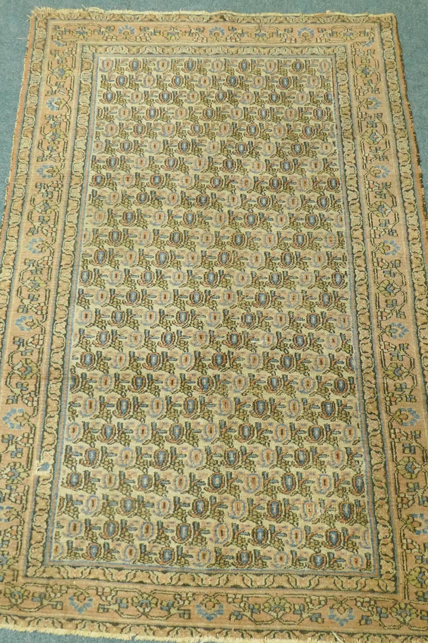 A Middle Eastern hand woven wool carpet with all over geometric designs on a faded terracotta field,