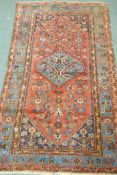An antique Middle Eastern hand woven wool carpet with blue borders and geometric designs on a red