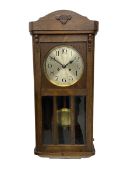 A 1930's wall clock in an oak case with a full-length door