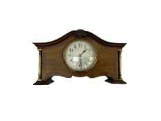 An Edwardian mantle clock in a mahogany case with a serpentine pediment and recessed brass pillars