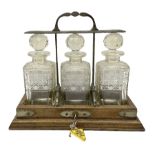 Edwardian oak tantalus with silver plated locking mechanism and three square sided glass decanters