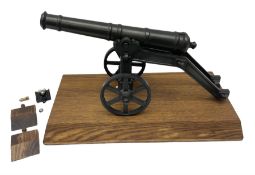 Black painted heavy cast metal model of a cannon on field carriage L41.5cm; loose mounted on oak bas