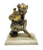 Brass figure of a knight seated up to a tree stump