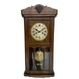 1930s wall clock in an oak case with a crested pediment and glazed door with visible pendulum