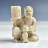 A Japanese ivory netsuke of a seated figure with a basket, 19th century, height 4cm, width 3cm.