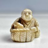 A Japanese ivory netsuke of a seated figure with basket, Meiji period, signed, height 3cm, width