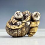 A Japanese ivory netsuke of two figures and a basket, Meiji period, height 3.5cm, width 4.5cm.