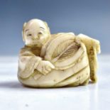 A Japanese ivory netsuke of a boy holding a palm leaf fan, Meiji period, height 2.7cm, width 3.4cm.